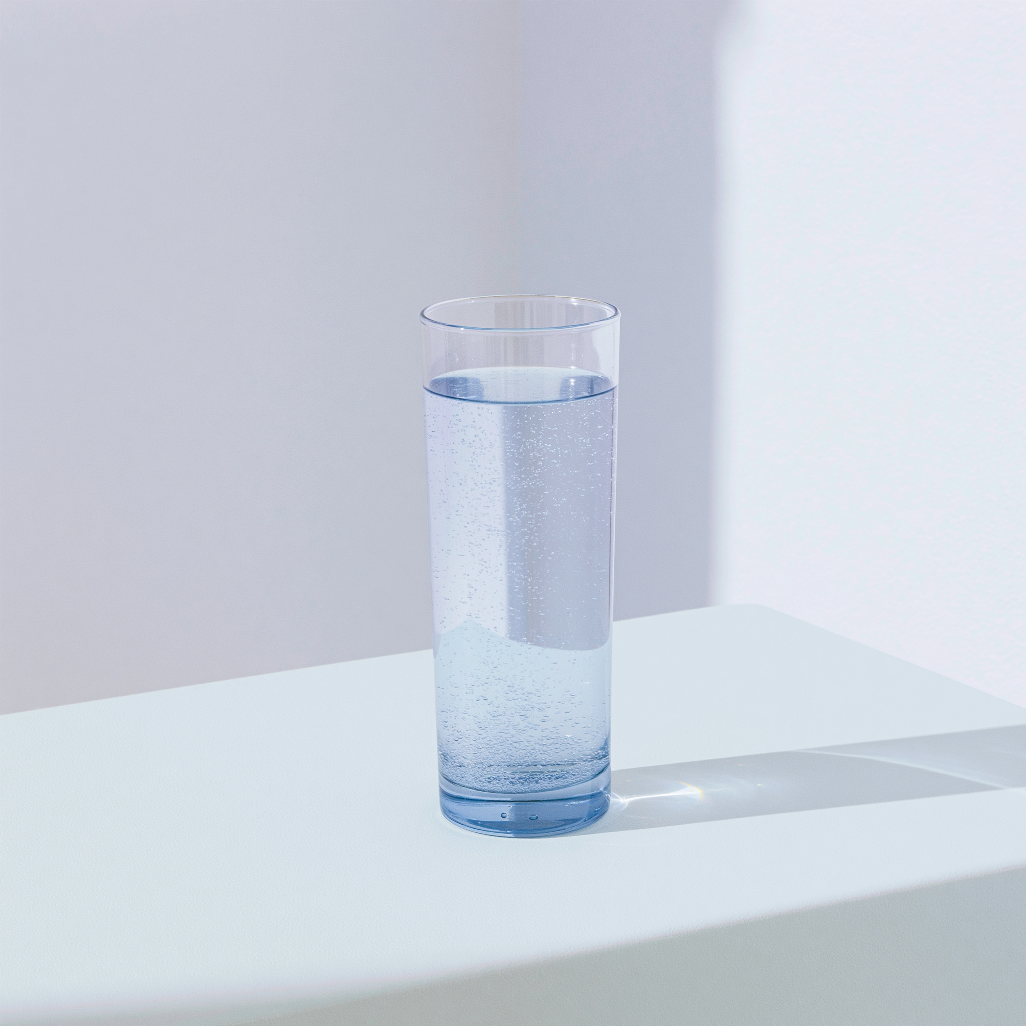 Un bicchiere d'acqua rosata su un tavolo, in luce chiara e diffusa